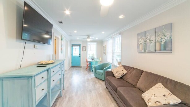 A living room with a sofa, a TV, a dining area with a table and chairs, and a door leading to another room.