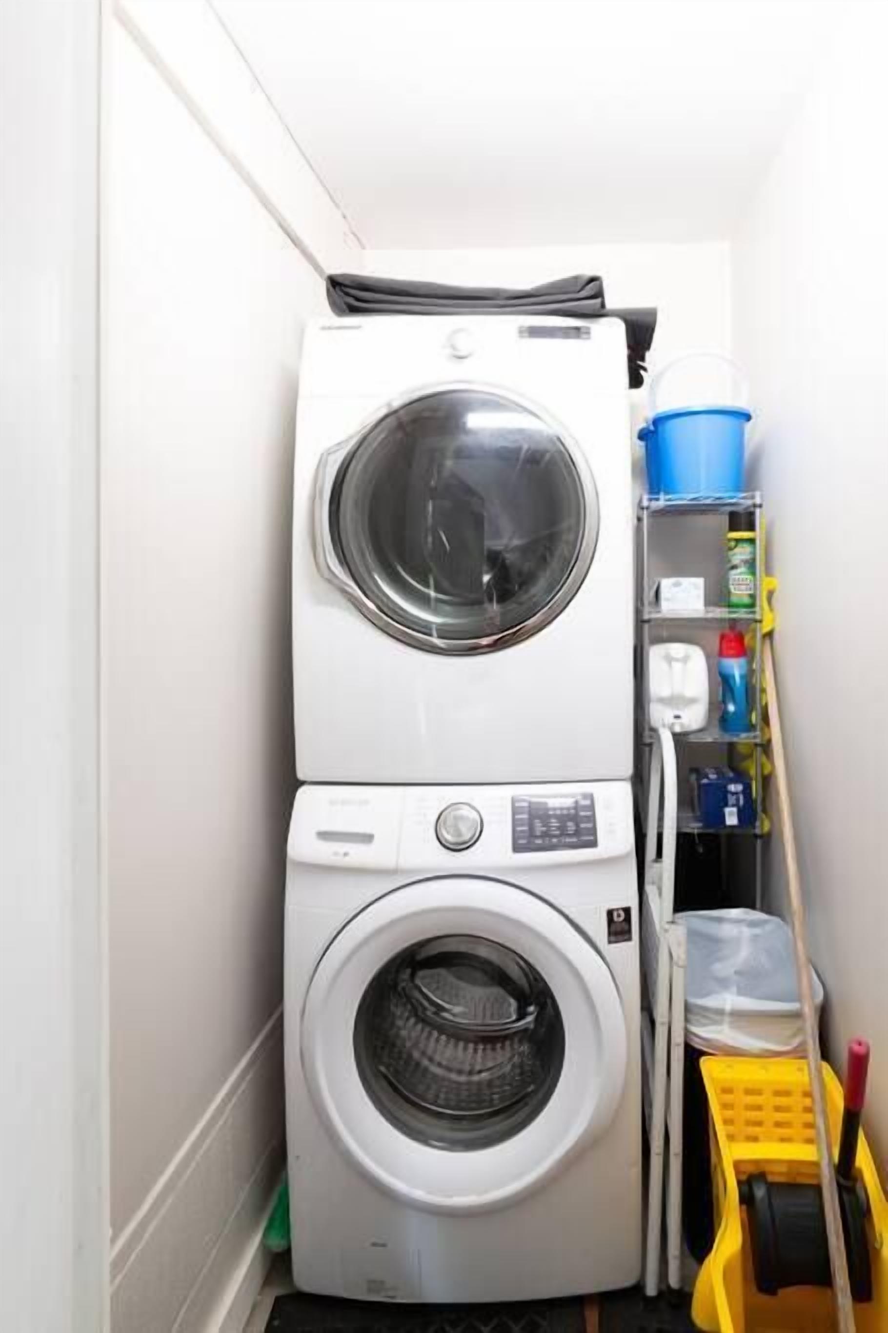 A compact laundry area with two stacked washing machines, a drying rack, and cleaning supplies.