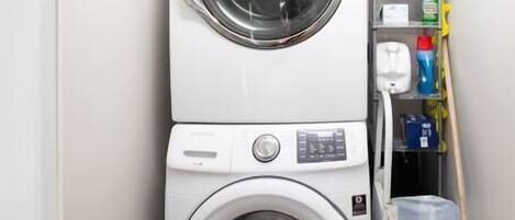 A compact laundry area with two stacked washing machines, a drying rack, and cleaning supplies.