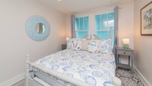 A bedroom with a bed, a nightstand, a mirror, and a window with curtains.