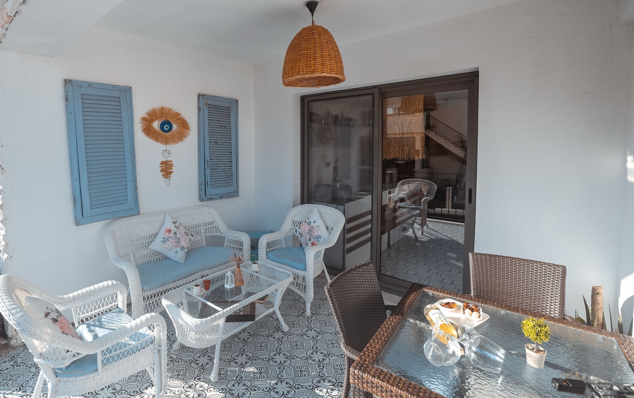 Una habitación con muebles de mimbre, una mesa de vidrio con copas de vino y vista a través de un ventanal.