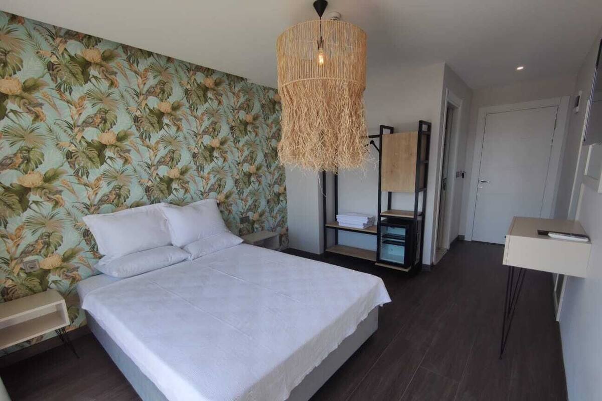 A bedroom with a large bed, a hanging light fixture, a wardrobe, and a bedside table.