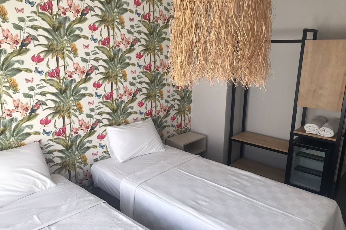 A room with two beds, a small table, and a wall with a floral pattern.
