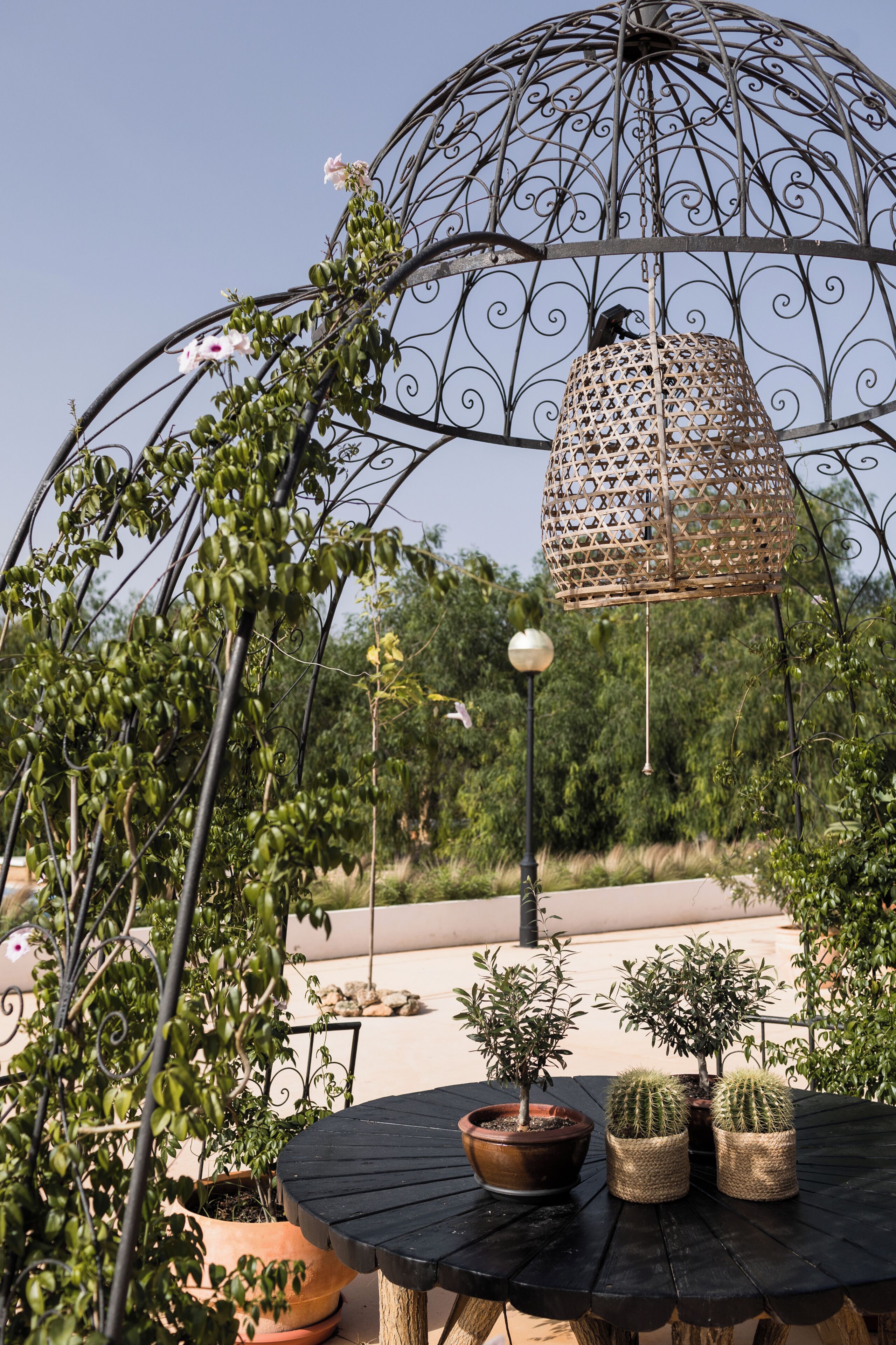A garden with a metal gazebo, potted plants, and a round table.