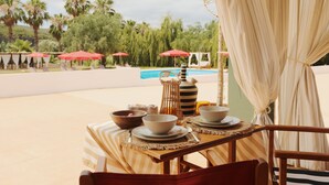 Uma mesa de jantar com tigelas e pratos, uma toalha listrada e vista para uma piscina e palmeiras.