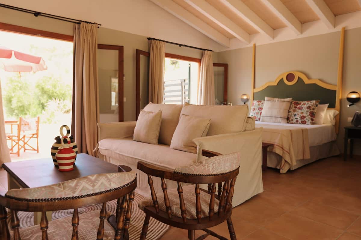 A room with a bed, a sofa, a wooden chair, a table, and a window with curtains.