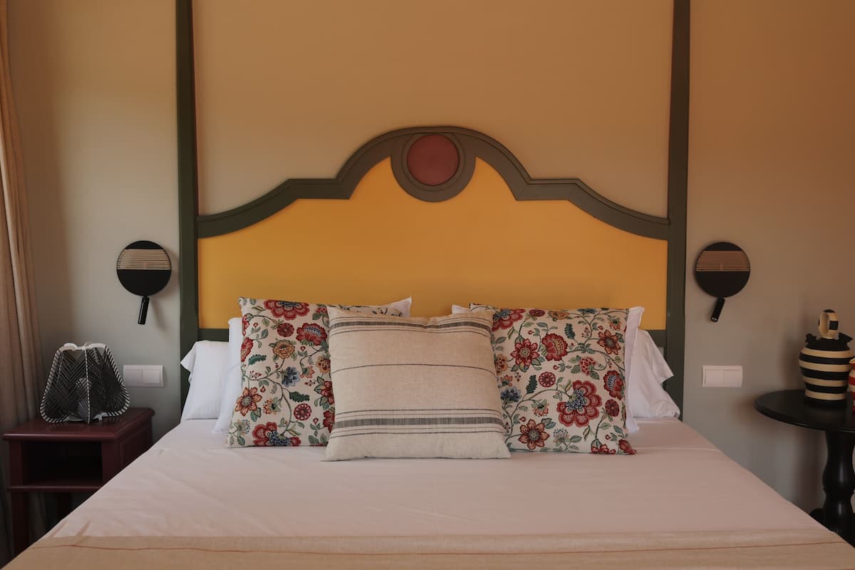 A neatly made bed with floral and striped pillows, a headboard with a circular accent, and a small table with a striped vase.