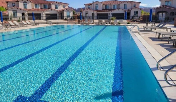 Ein klares Schwimmbecken mit Bahnen, umgeben von Liegestühlen und einem Zaun.