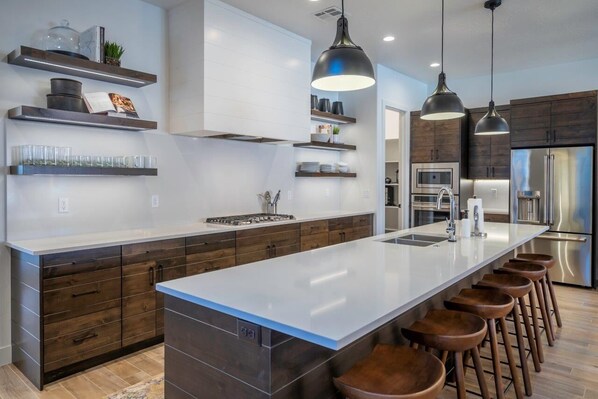 A modern kitchen with a large island, dark wood cabinets, and stainless steel appliances.