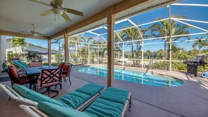 A covered pool area with lounge chairs, a table, and chairs. - Lazy Daze - 5 Bedroom, Sofa Bed-3.5 Bath-Private House-Heated Pool-Waterfront (Cape Coral)