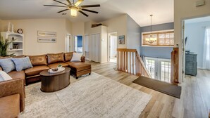 A spacious living room with a brown leather sofa, a wooden coffee table, and a ceiling fan. There is a staircase leading to an upper level with a view of the outside. - Lazy Daze - 5 Bedroom, Sofa Bed-3.5 Bath-Private House-Heated Pool-Waterfront (Cape Coral)
