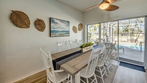 A dining area with a wooden table, white chairs, and a ceiling fan. - Lazy Daze - 5 Bedroom, Sofa Bed-3.5 Bath-Private House-Heated Pool-Waterfront (Cape Coral)