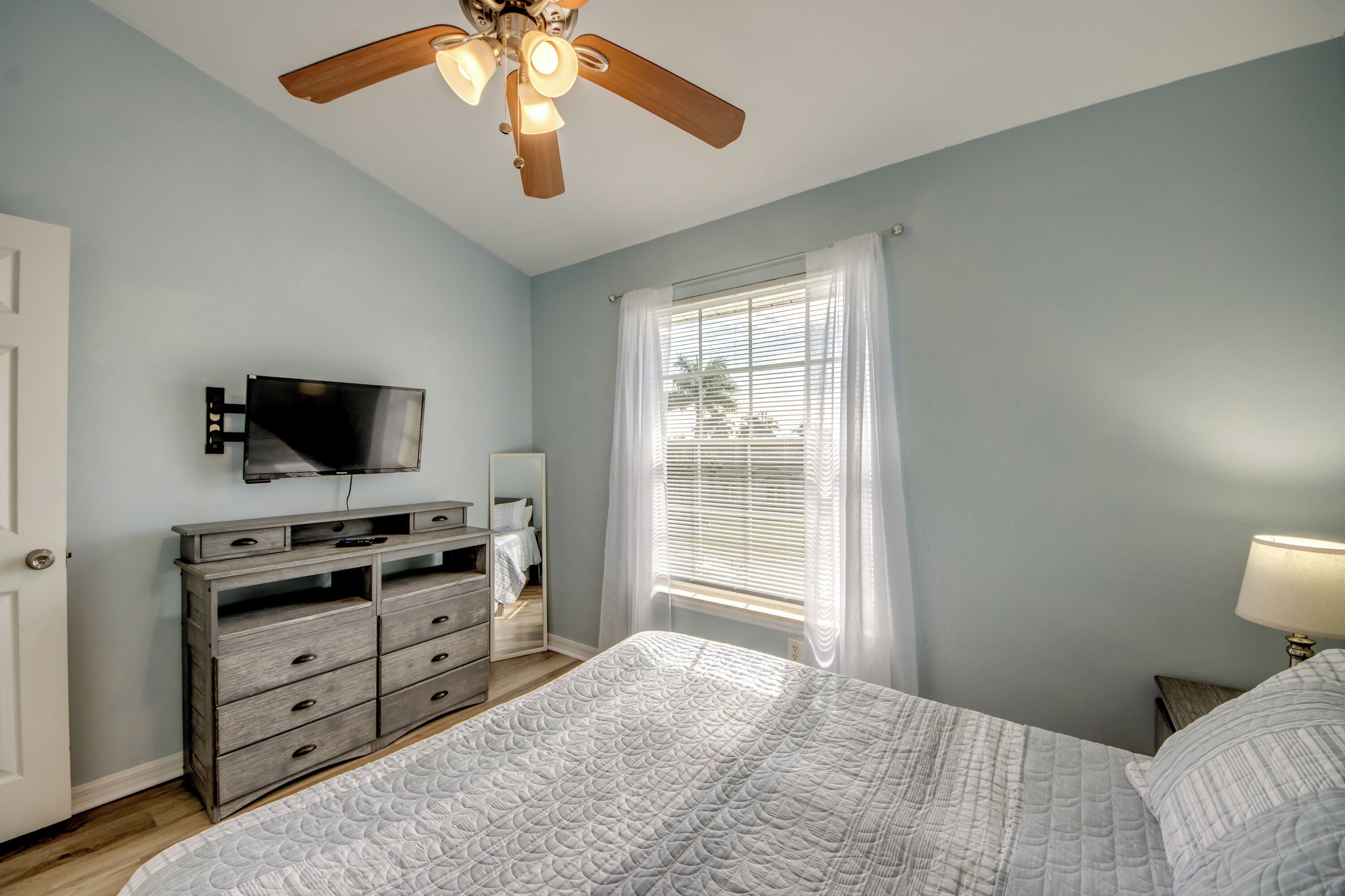 A bedroom with a bed, a dresser, a TV, and a ceiling fan.