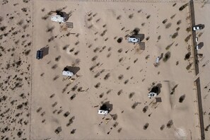 An aerial view of a desert area with several small buildings, some with attached vehicles, and a road running parallel to the buildings. - JT Village Campground - Lil Miss Daisy (Joshua Tree)