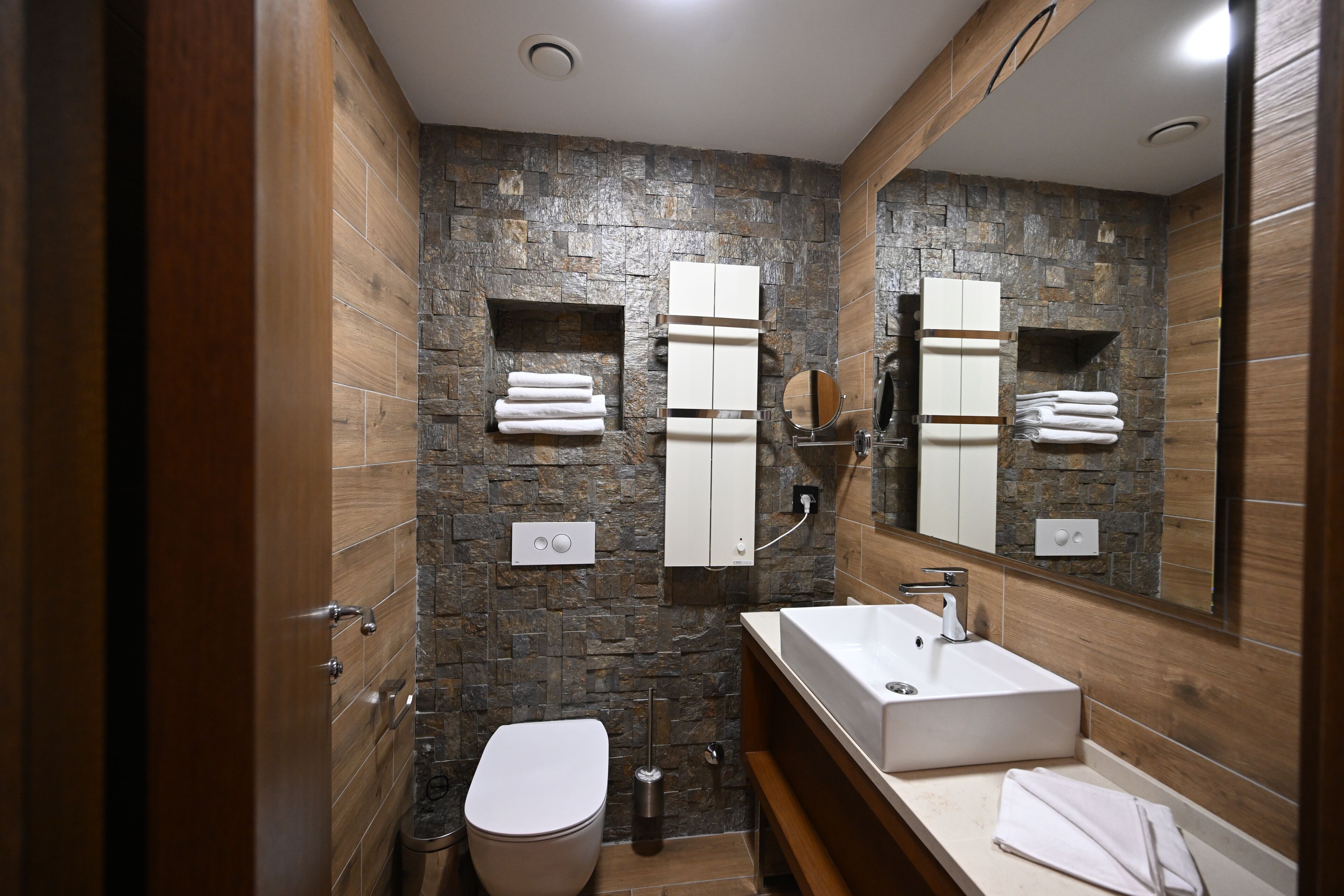 Ein modernes Badezimmer mit Steinwand, Holzwaschtisch, weißem Waschbecken und Toilette.