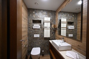 A modern bathroom with a stone wall, wooden vanity, a white sink, and a toilet. - Hotel Tamis (Pancevo)