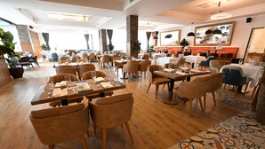 Un restaurante espacioso con varias mesas y sillas, ventanas amplias y un corredor con estampado en el suelo.