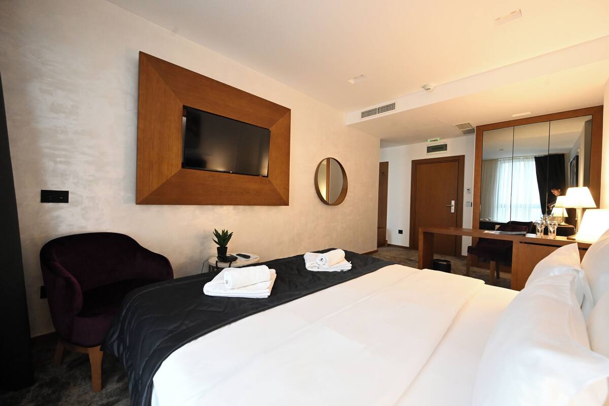 Une chambre d’hôtel avec un grand lit, un bureau, une chaise, un téléviseur fixé au mur et un miroir.