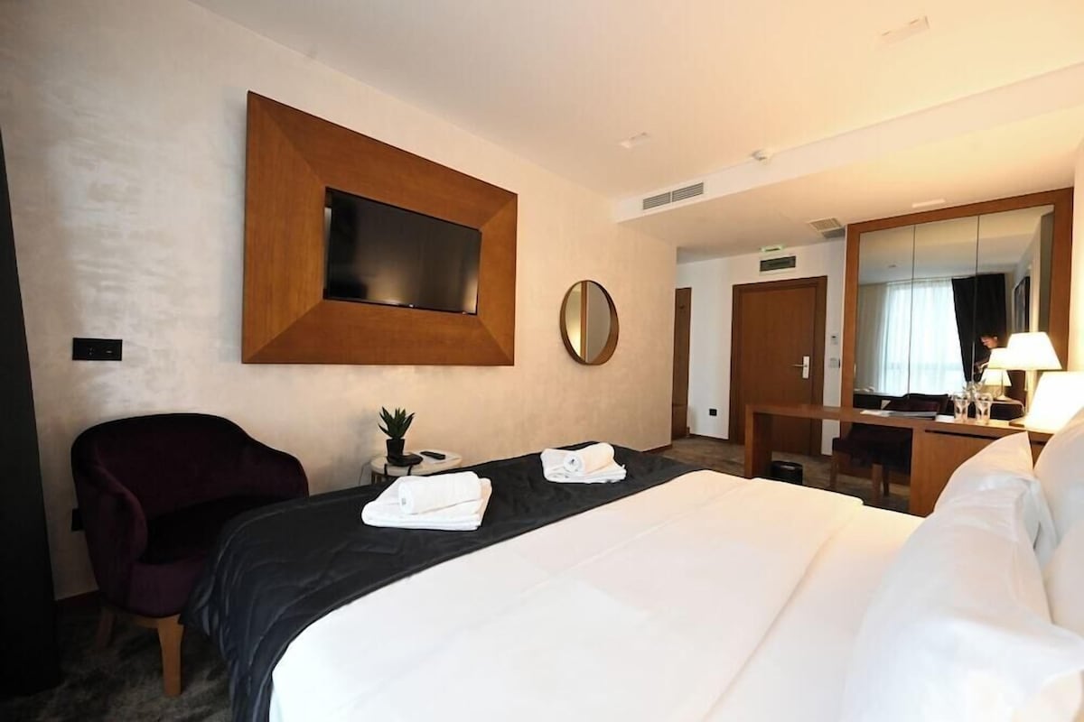 A hotel room with a bed, a desk, a chair, a mirror, and a television.