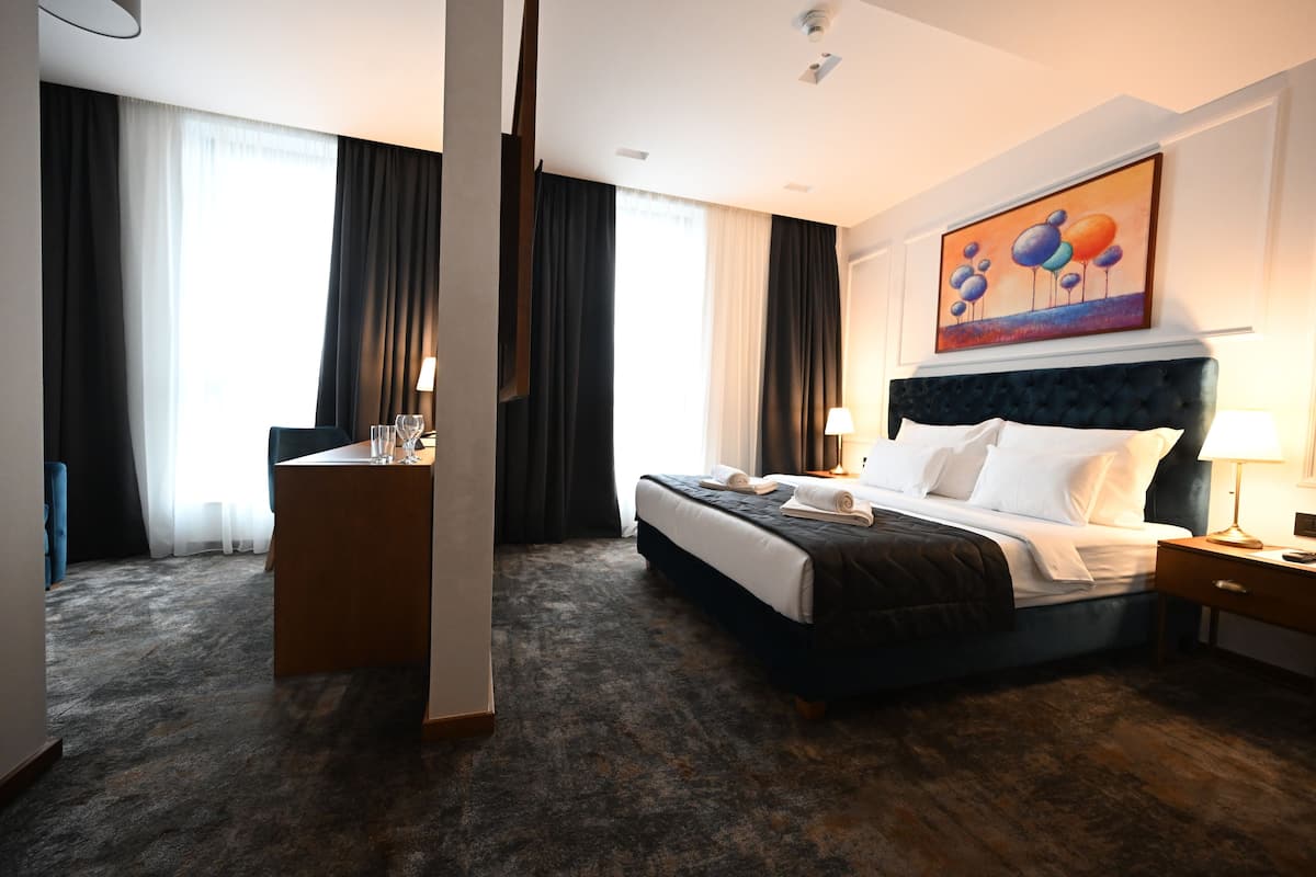 Une chambre d’hôtel avec un grand lit, un bureau avec une chaise, une table de chevet et un tableau au mur.