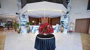Una zona de recepción con un mostrador de mármol, un gran arreglo floral y una escalera dorada.