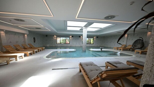 Un spa con una amplia piscina interior, tumbonas y un diseño de techo moderno.