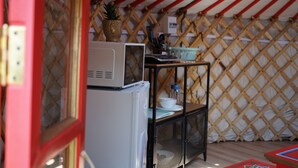 Una kitchenette funcional con microondas, un refrigerador pequeño y una estantería metálica con utensilios de cocina.