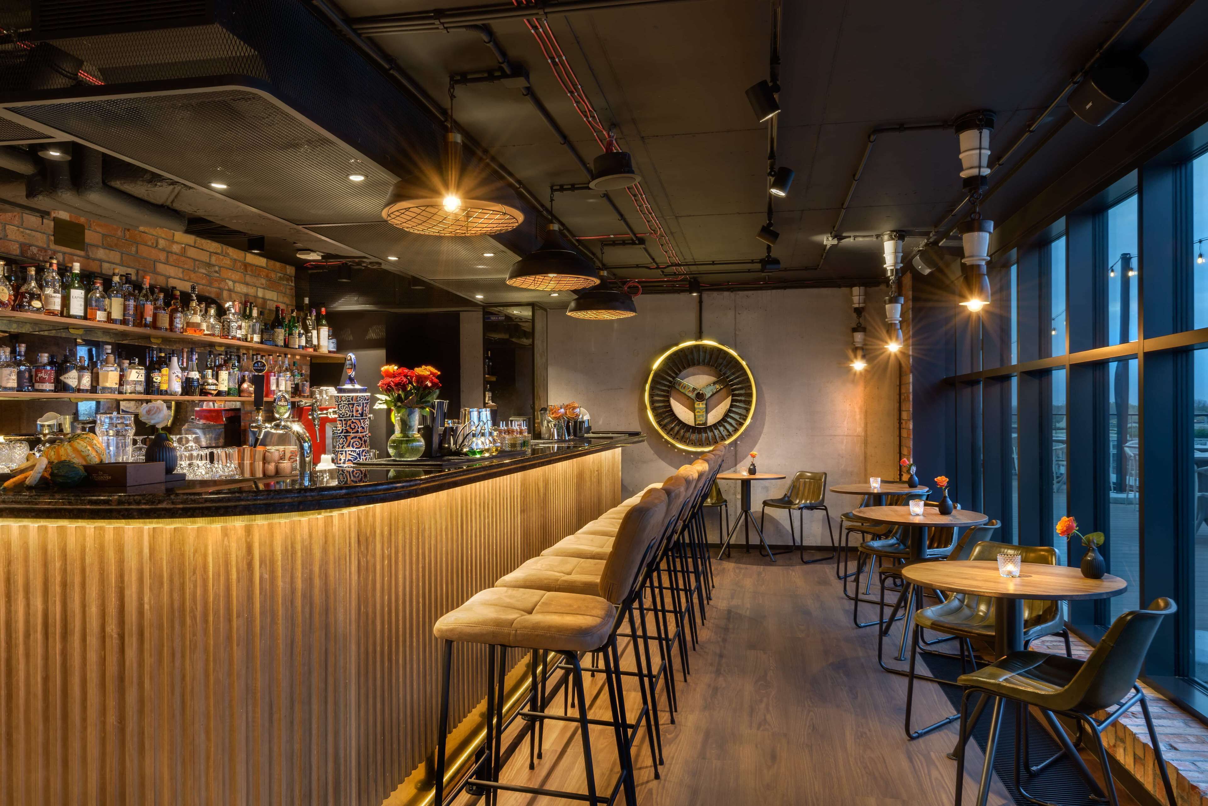 A bar area with a wooden counter, stools, and tables. There are bottles and glasses on the shelves.