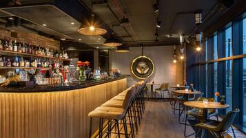 A bar area with a wooden counter, stools, and tables. There are bottles and glasses on the shelves.