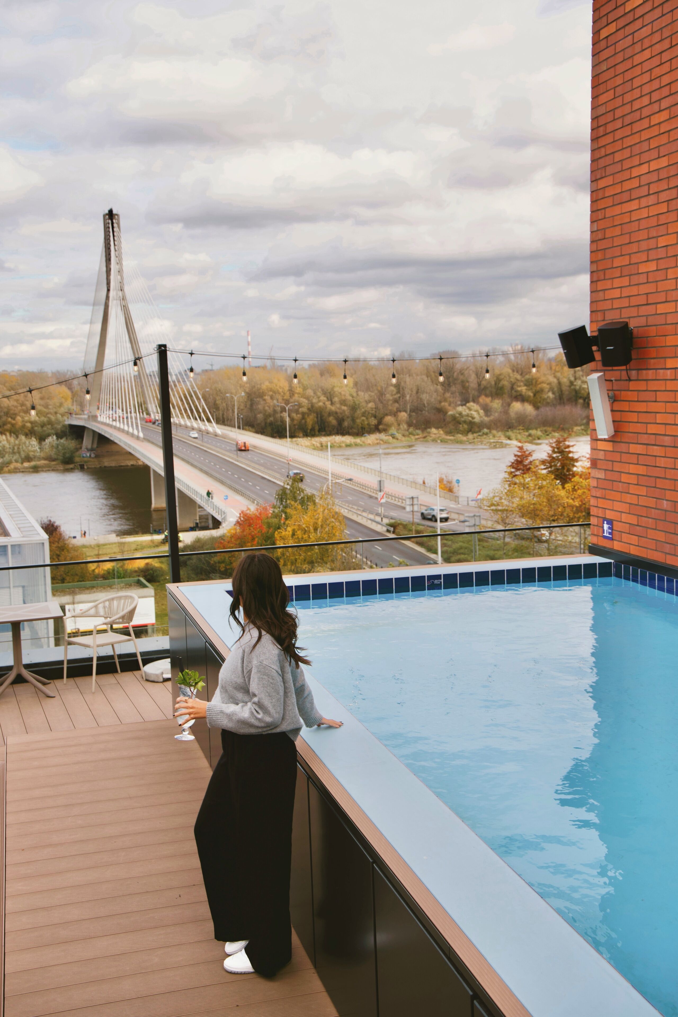 A person standing by a pool with a view of a bridge and river.