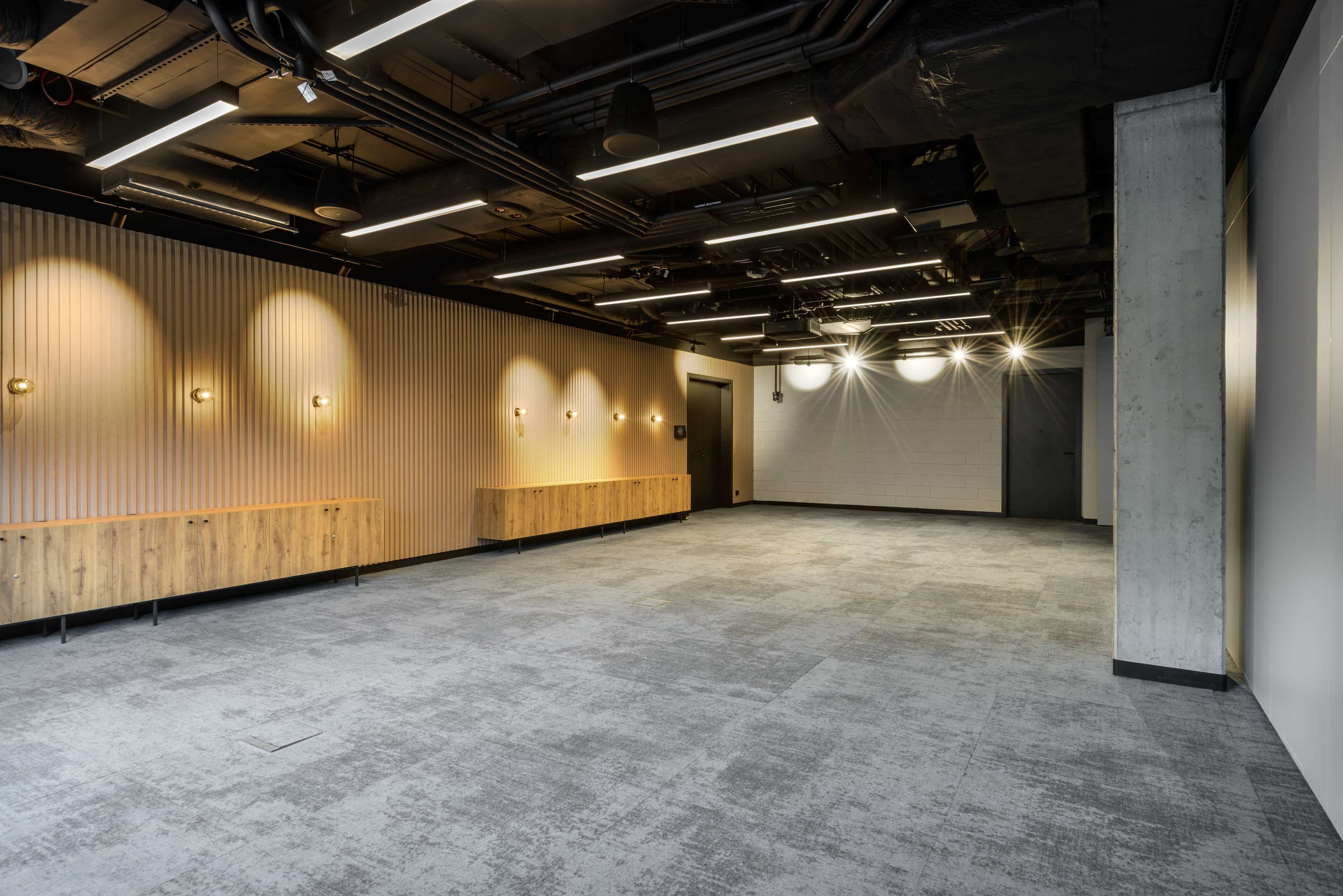Een ruime, moderne binnenruimte met een gepolijste betonvloer, houten wandbekleding en inbouwverlichting.