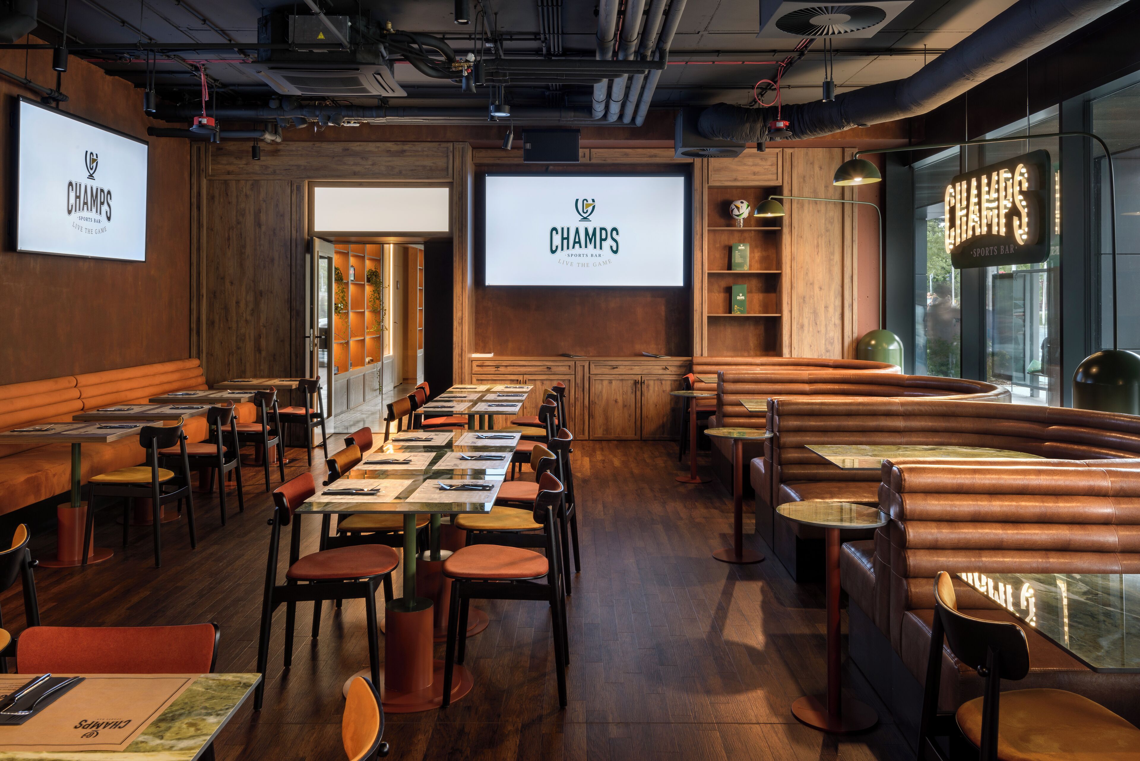 Eine Sportsbar mit mehreren Sitzbereichen, darunter Boxsitzgelegenheiten und Tische, und einem großen Bildschirm, der das Logo der Bar zeigt.