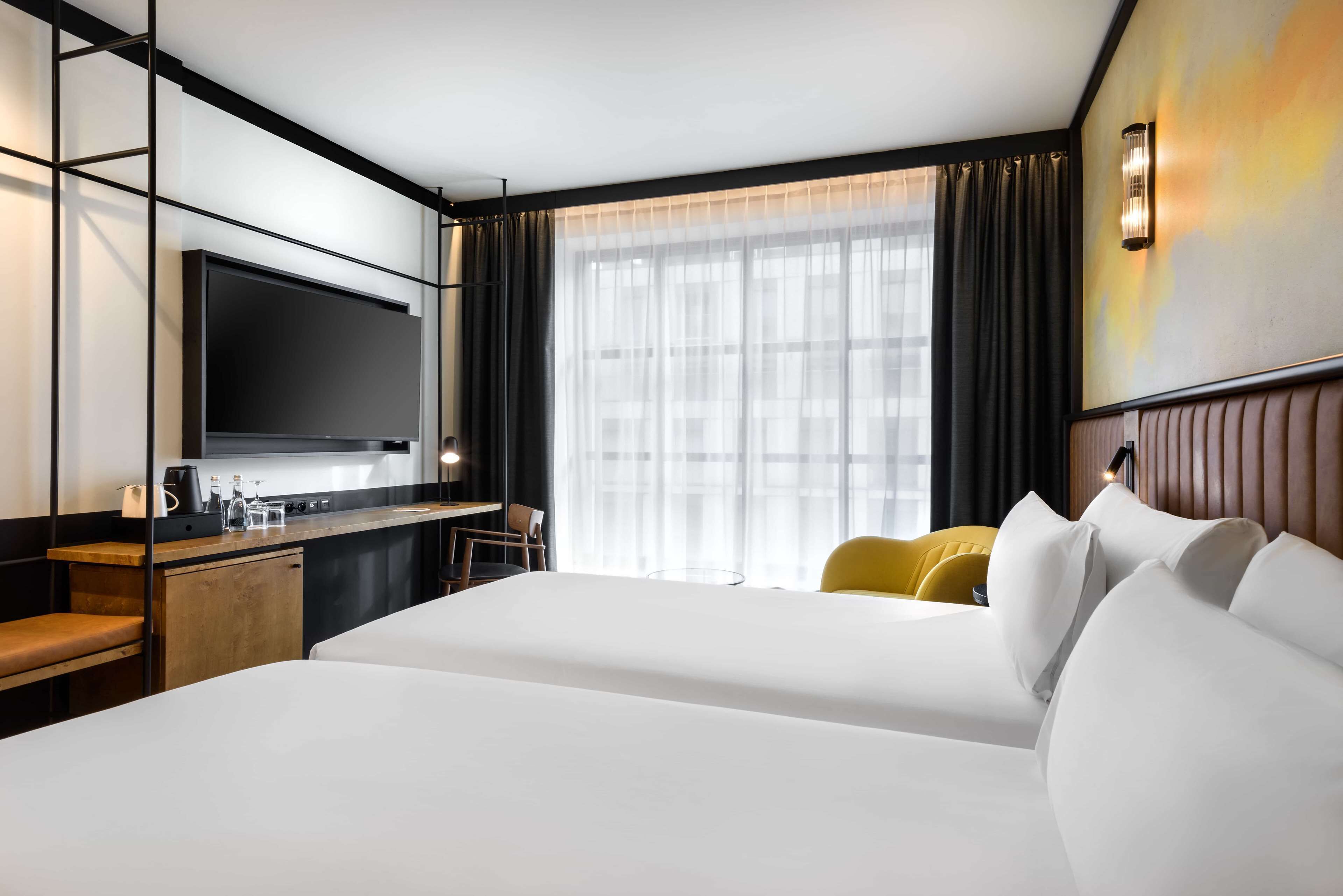 Une chambre d’hôtel avec un grand lit, un bureau doté d’un téléviseur à écran plat, une machine à café et un petit coin salon avec des chaises jaunes.