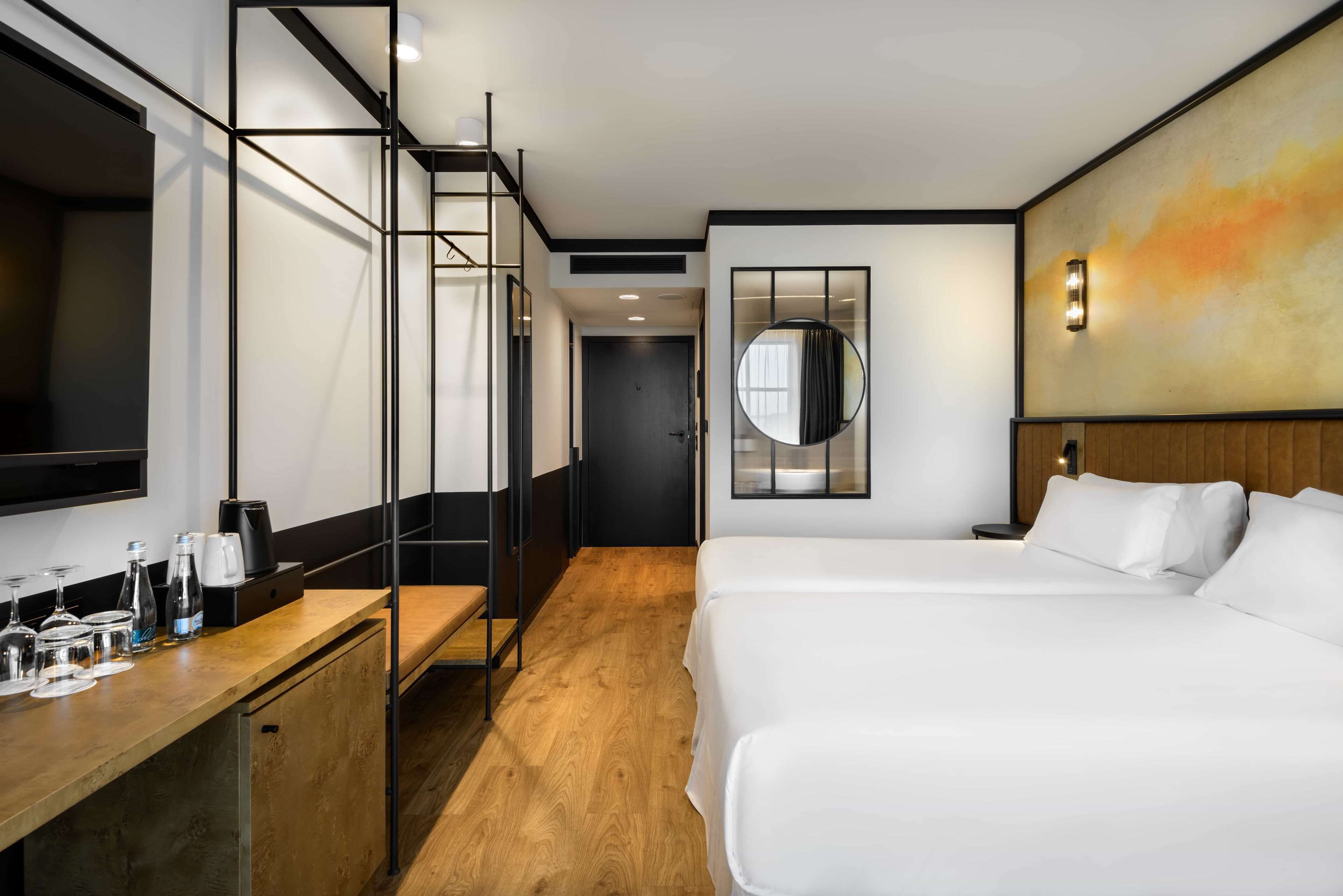 Une chambre d’hôtel moderne avec un grand lit, un bureau doté d’une machine à café, un miroir et un tableau au mur.
