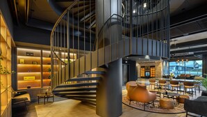 A modern interior with a spiral staircase, seating area, and a reception desk. - Barceló Warsaw Powiśle (Warsaw)