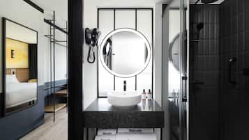 Un baño moderno con un espejo redondo, un lavabo y una zona de ducha.