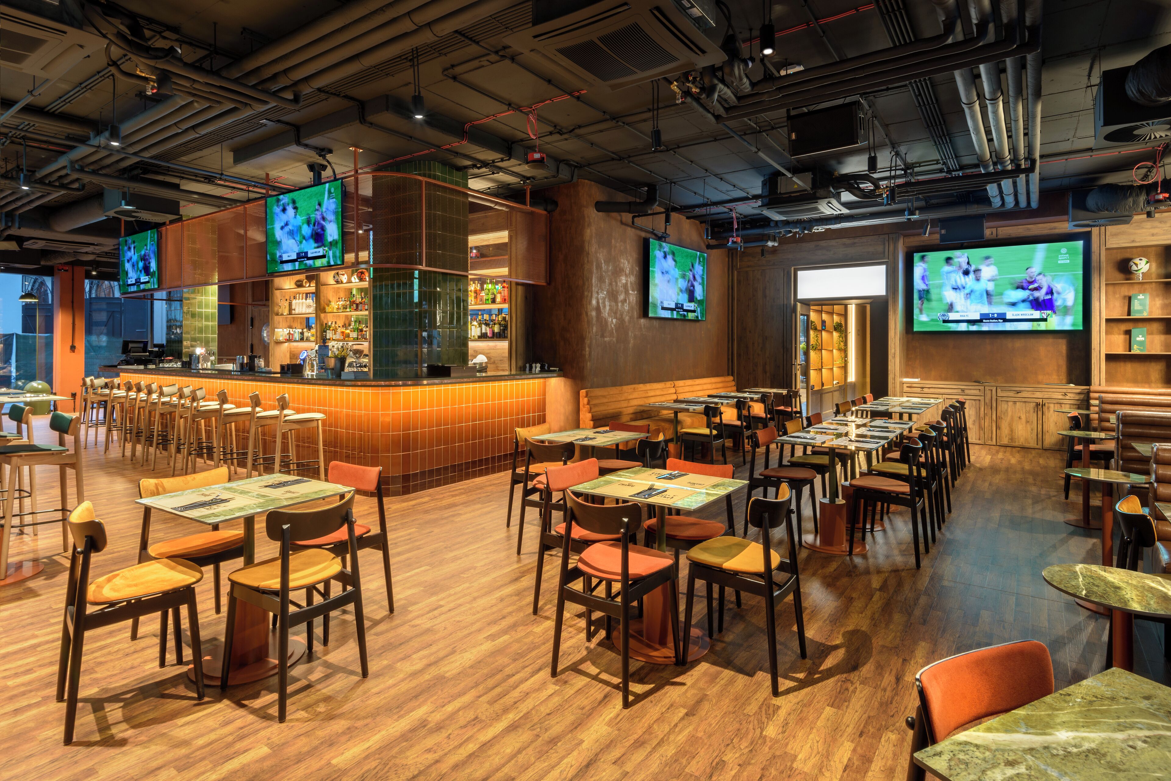 Un restaurante con varias mesas y sillas, una zona de bar y varios televisores mostrando eventos deportivos.