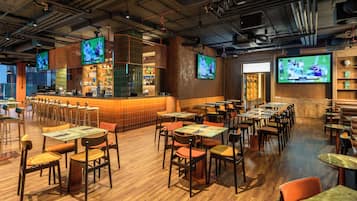Un restaurante con varias mesas y sillas, una zona de bar y varios televisores mostrando eventos deportivos.