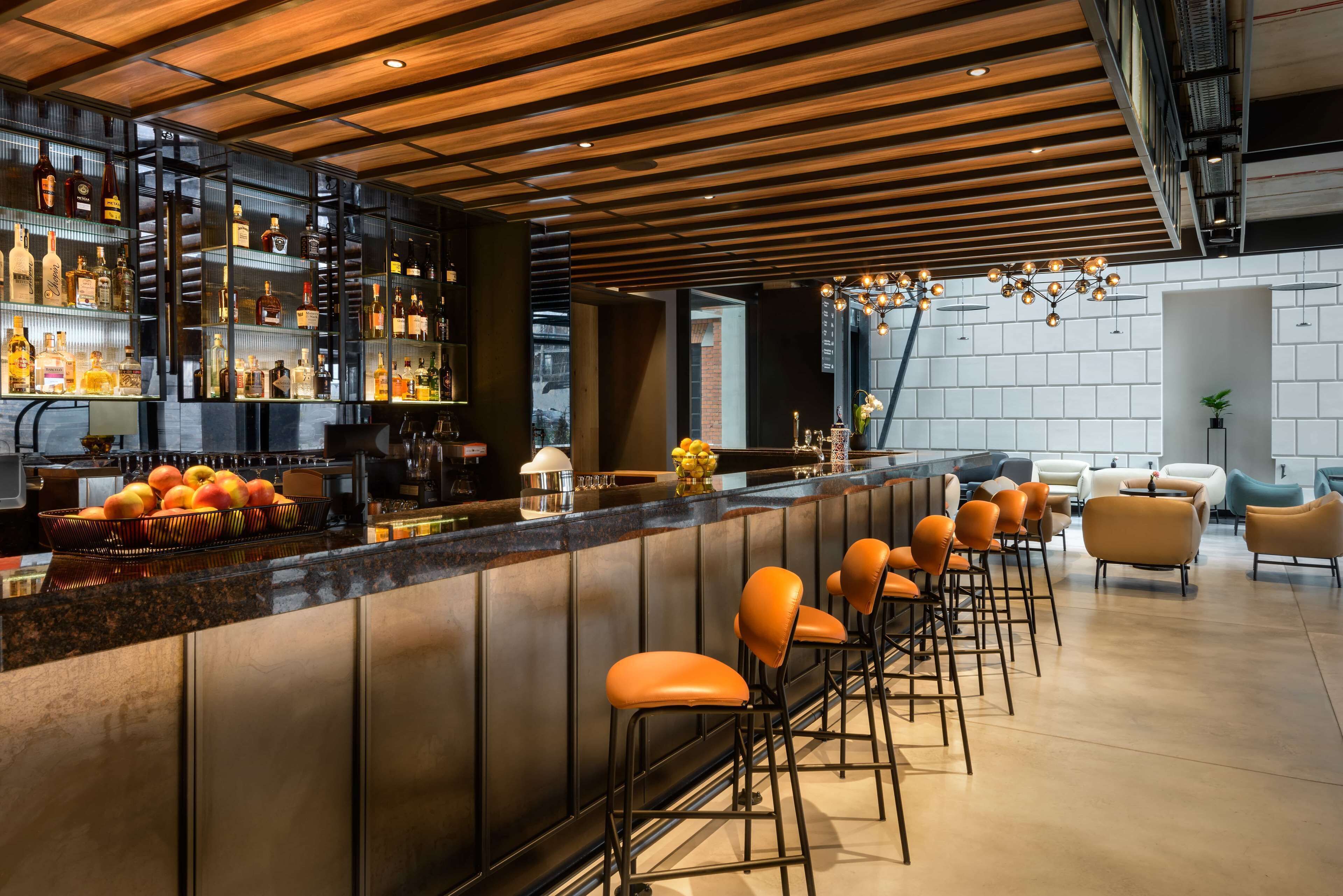 A modern bar area with a wooden ceiling, bar stools, and a variety of bottles on shelves.