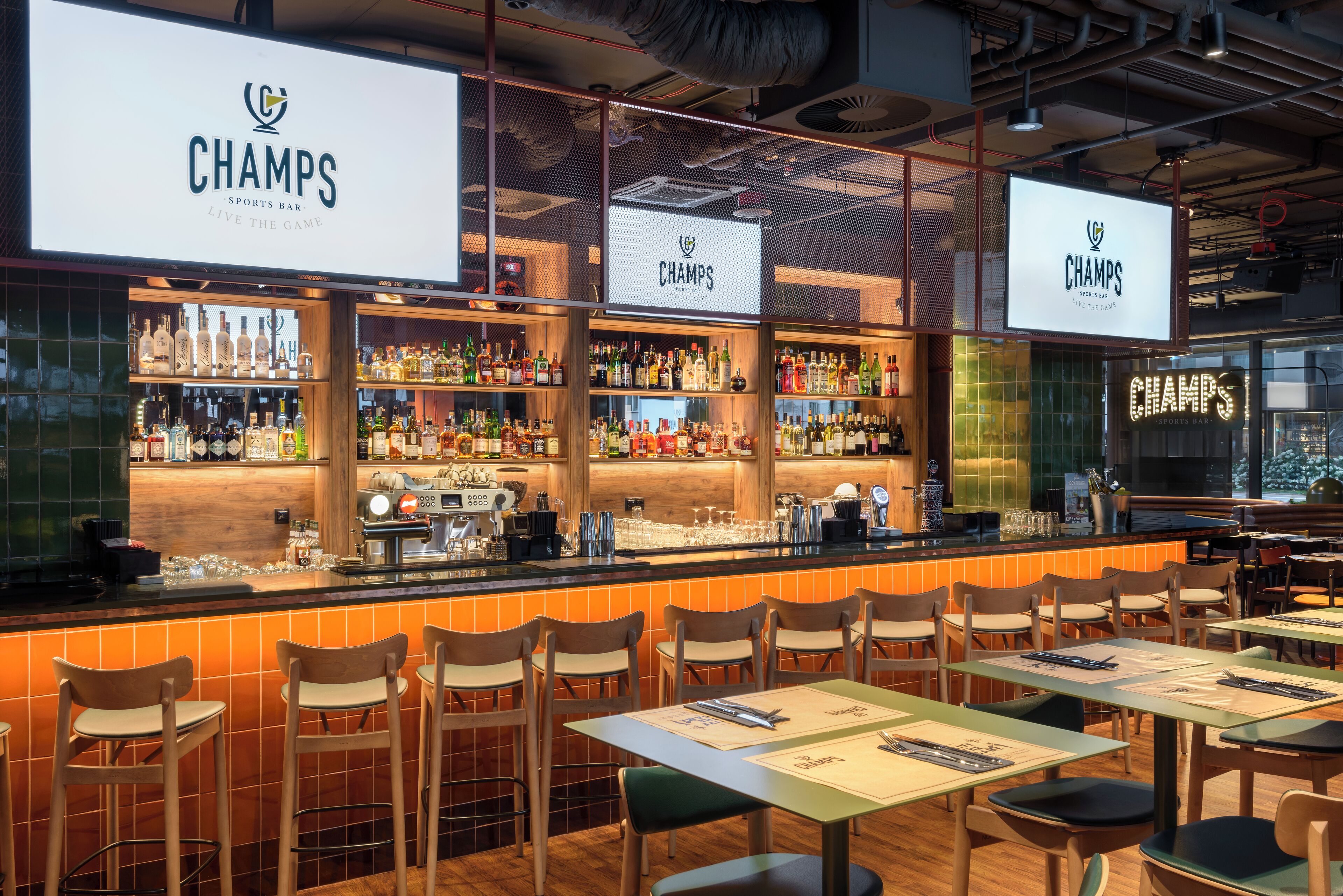 Een sportbar interieur met meerdere zithoeken, een bar met een divers aanbod aan flessen, en een grote verlichte reclamebord.
