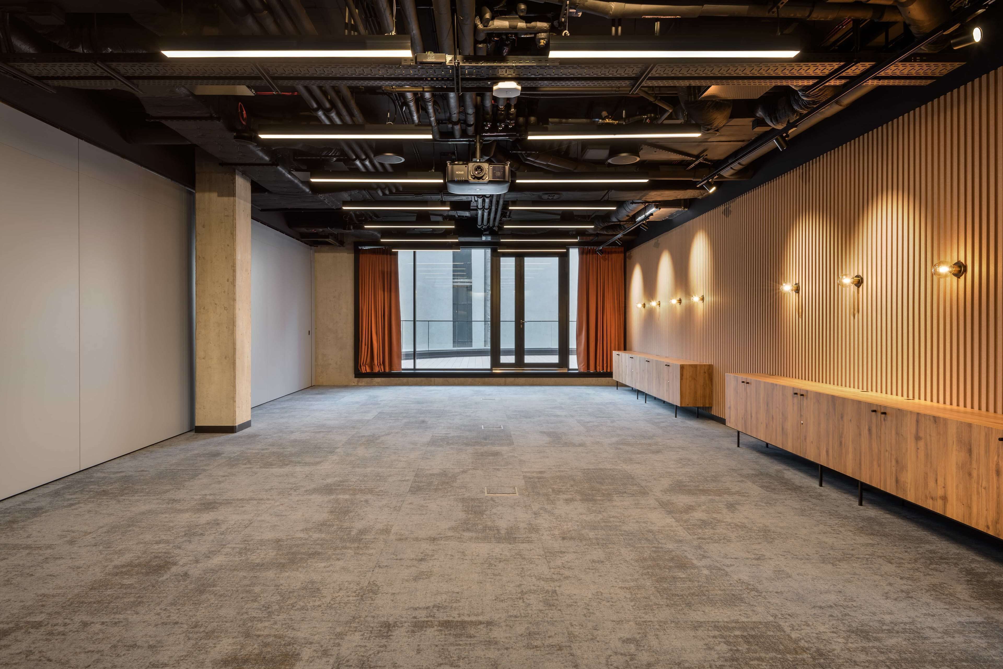 A conference room with a high ceiling, exposed ductwork, and a large window with curtains.