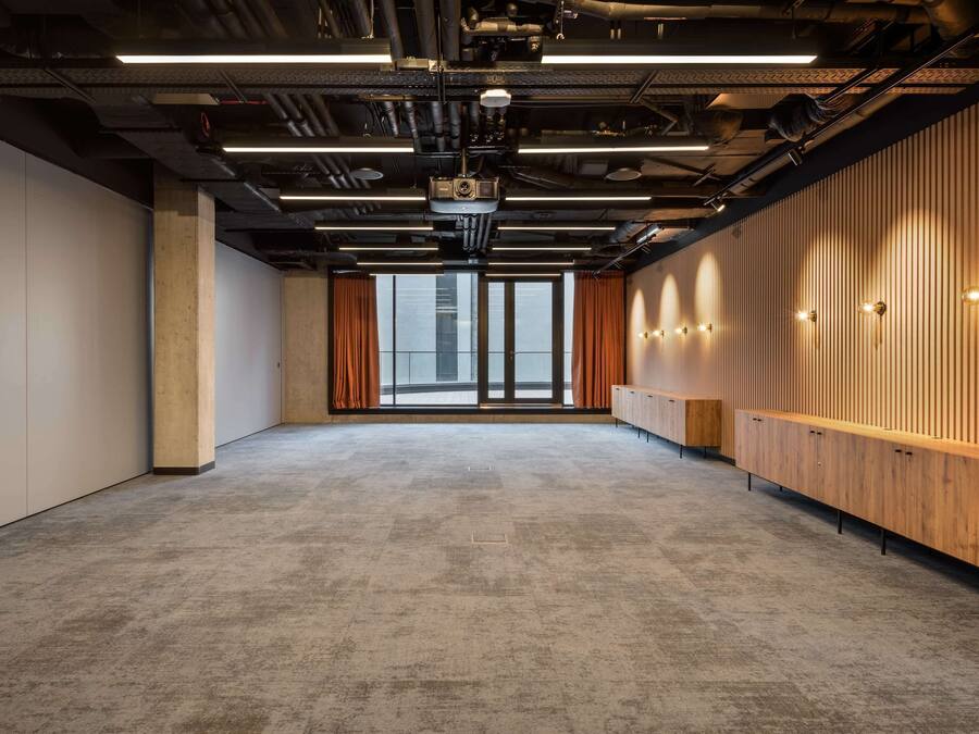 A conference room with a high ceiling, exposed ductwork, and a large window with curtains.