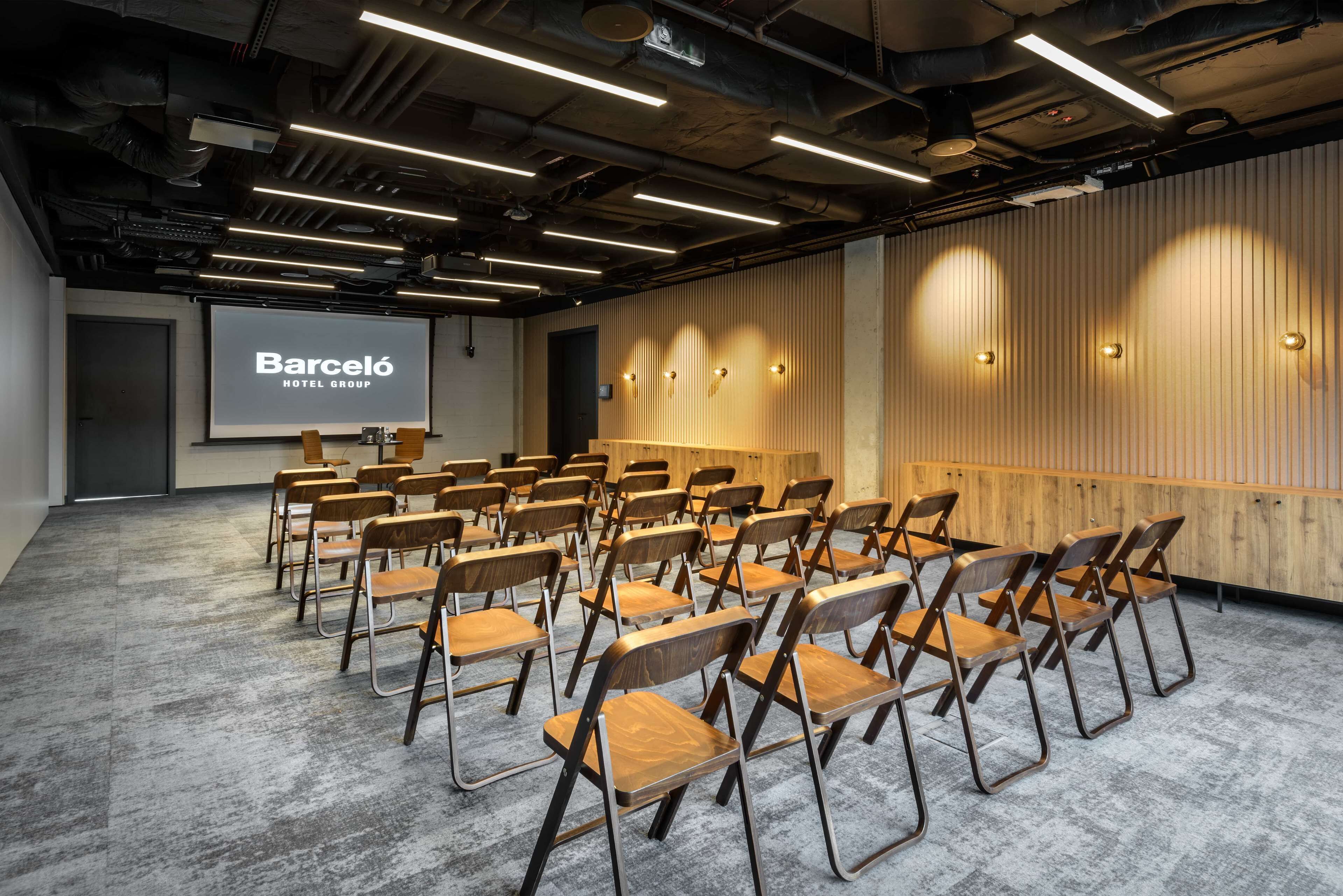 Une salle de conférence avec des rangées de chaises, un écran de projection et un mur recouvert de panneaux en bois.