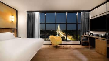 A hotel room with a large bed, a desk, a chair, and a view of a bridge at night.