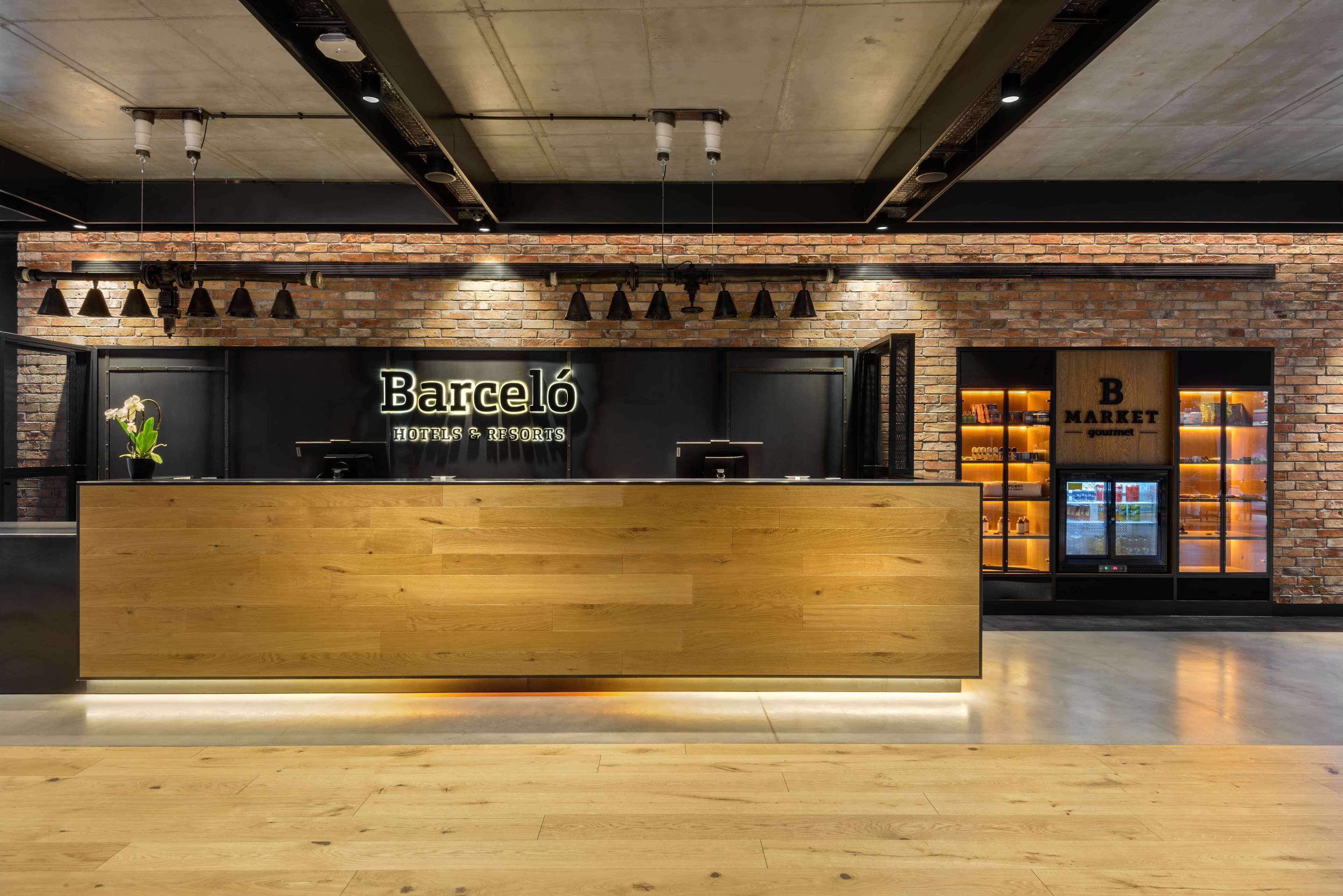 A Barcelona hotel reception with a wooden counter, brick walls, and a B Market gourmet section.