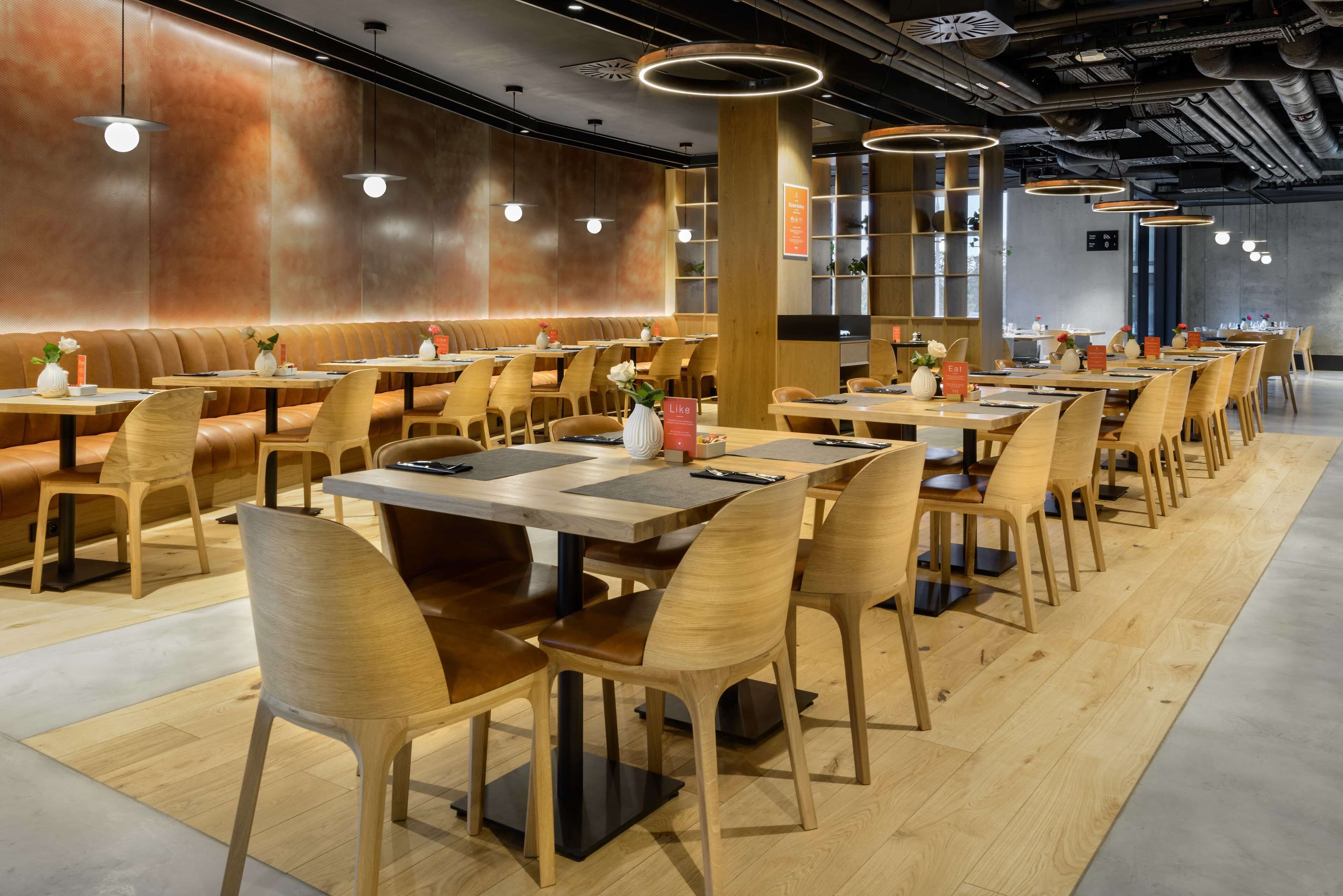 Un restaurante moderno con mesas y sillas de madera, una barra larga e iluminación colgante.