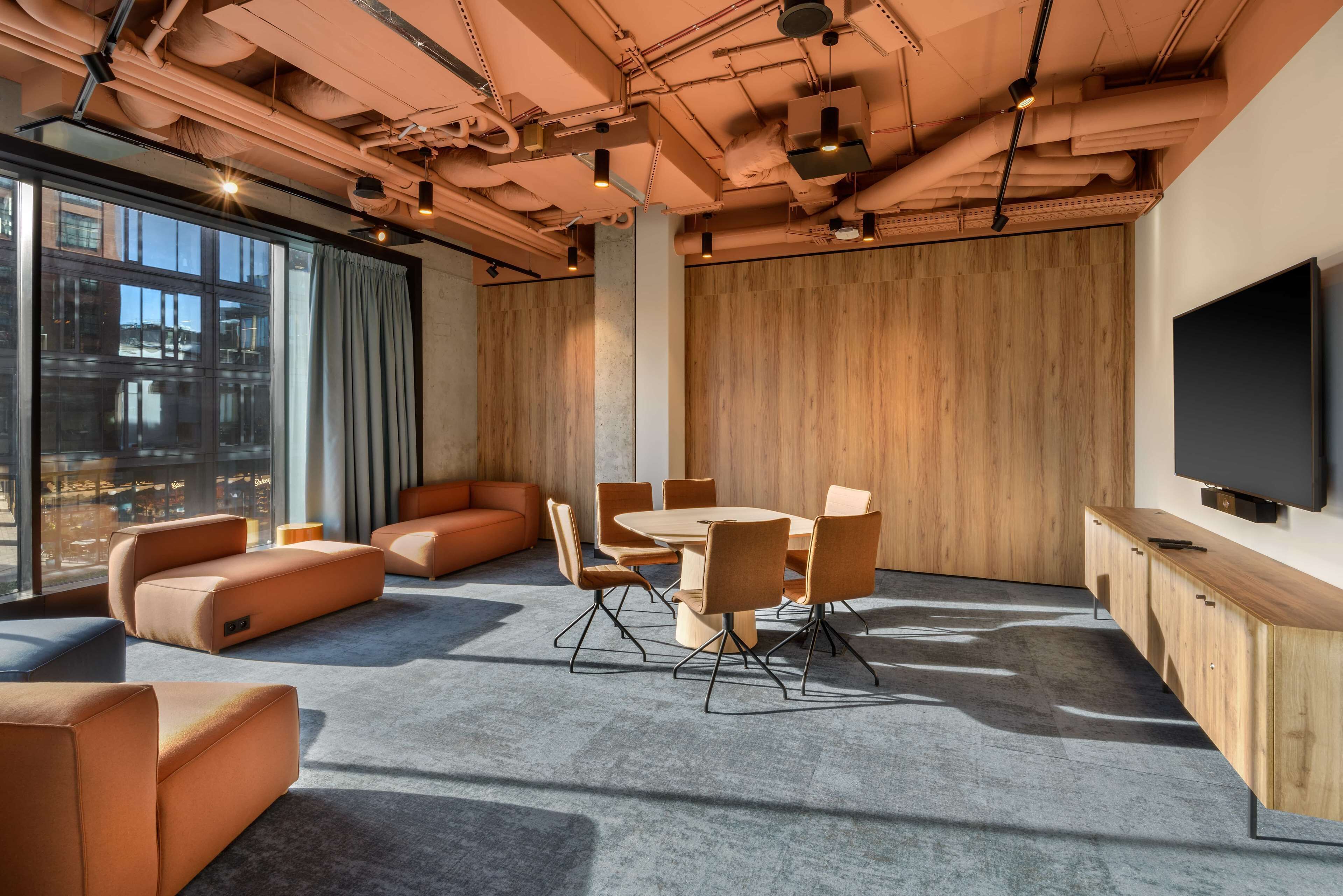 Une salle de réunion moderne, dotée d’une grande table, de sièges confortables et d’un téléviseur fixé au mur.