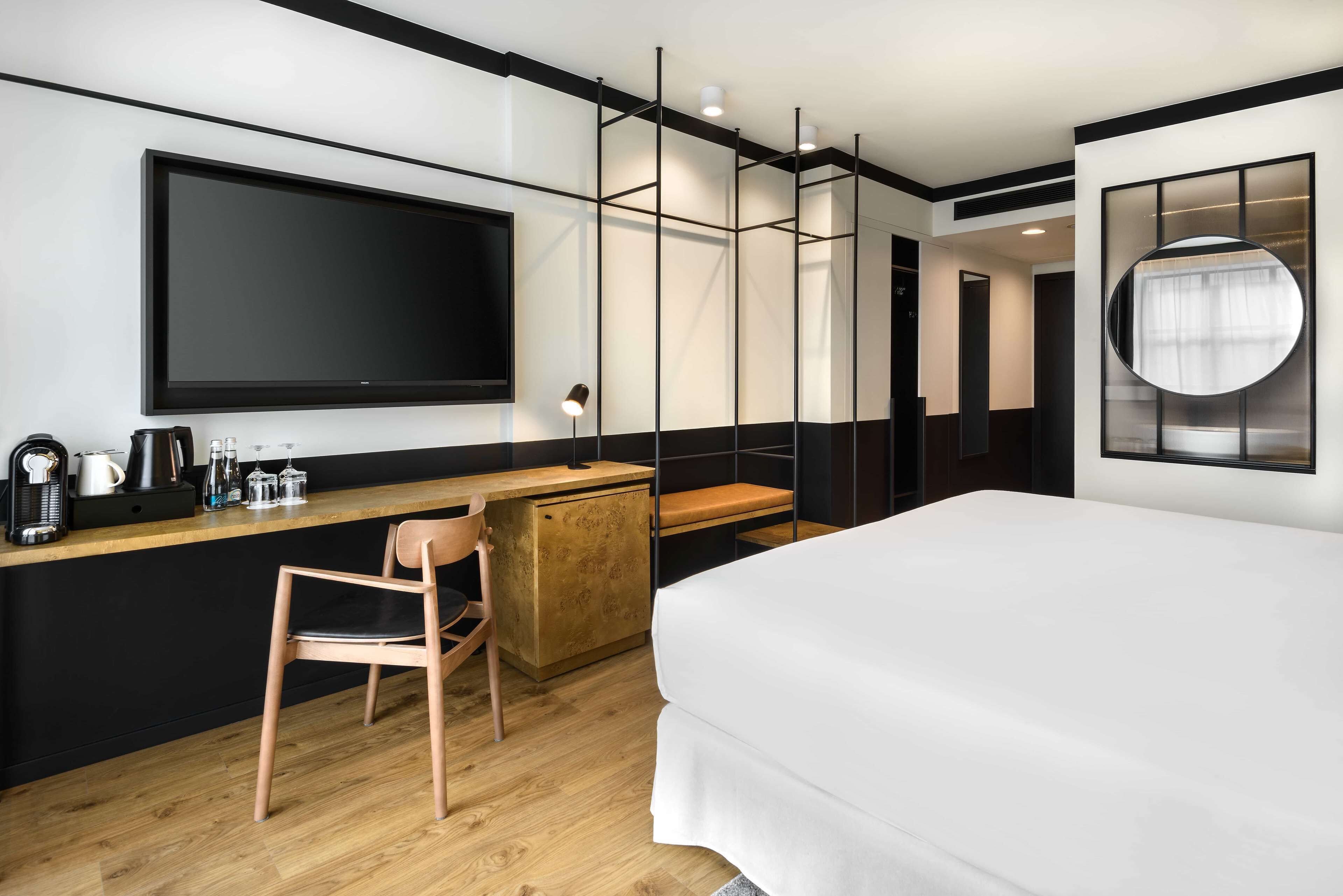 Une chambre d’hôtel moderne dotée d’un grand lit, d’un bureau avec une chaise, d’une télévision à écran plat et d’un miroir rond.