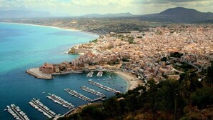 Una ciudad costera con un puerto deportivo, edificios históricos y montañas al fondo.