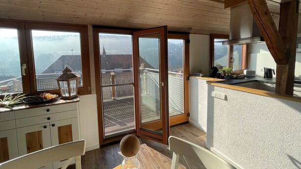 A modern kitchen with wooden beams, large windows, and a view of a cityscape.